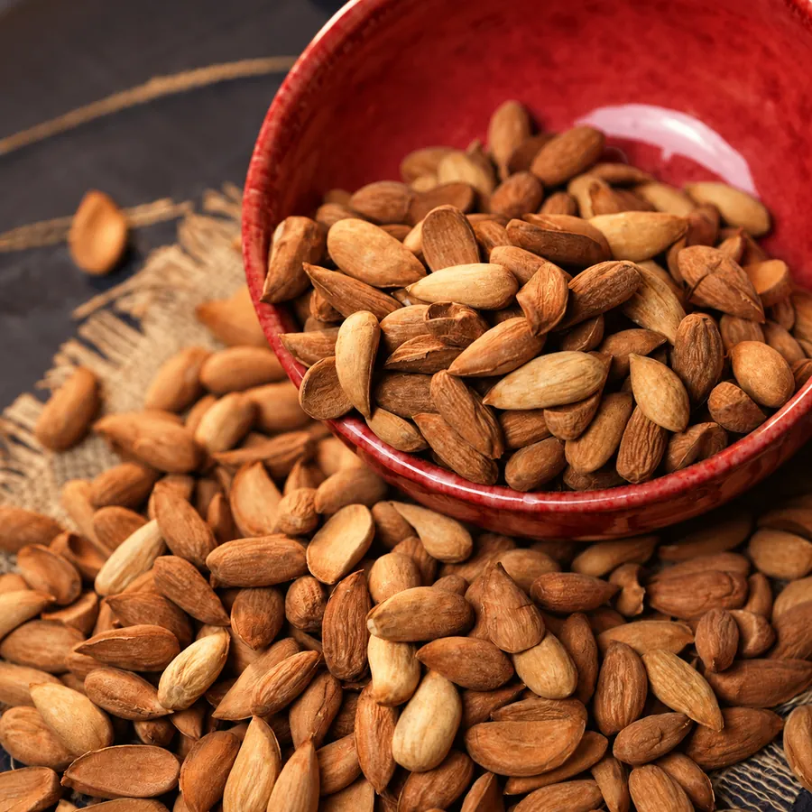 Shelled almonds spilling from a red ceramic bowl onto burlap