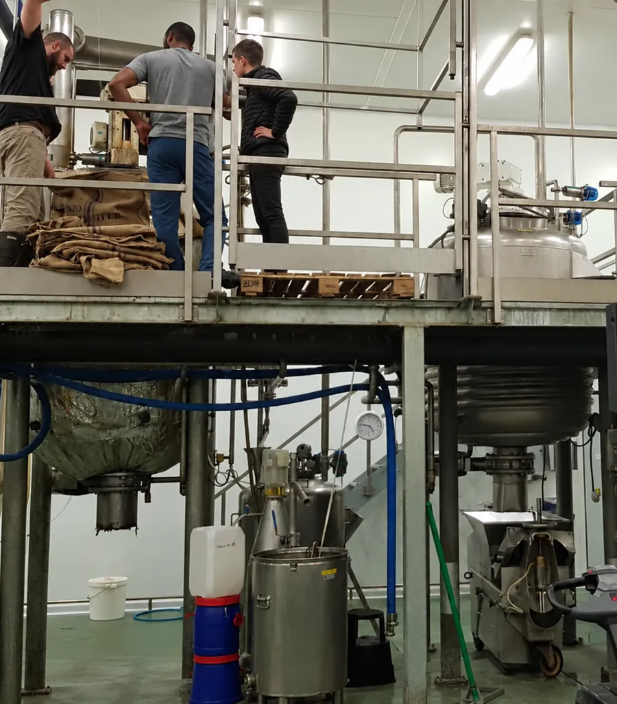 Technicians loading jute sacks of raw botanical material into stainless-steel processing vessels